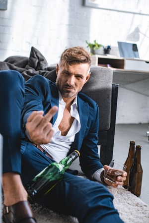drunk businessman showing middle finger and holding glass with alcohol drinkの写真素材