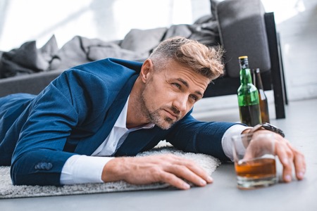 selective focus of drunk businessman lying on carpet near glass with alcohol drinkの写真素材