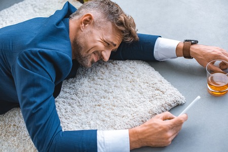 drunk businessman lying on carpet with smartphone in handの写真素材