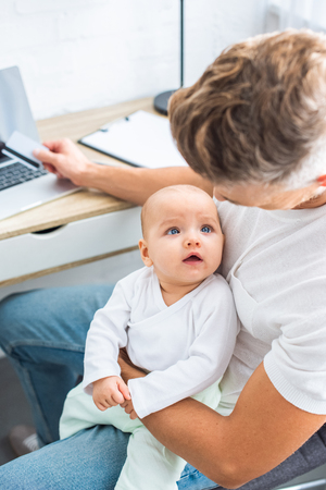 father sitting at computer desk with credit card and looking at baby daughterの写真素材