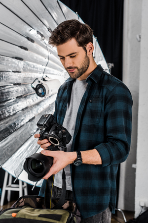 handsome young photographer holding professional photo equipment in studioの写真素材
