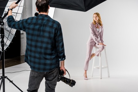 back view of photographer holding camera and model posing in studioの写真素材