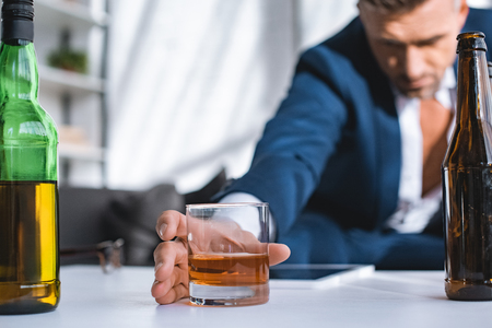 selective focus of glass with whiskey in hand of drunk businessmanの写真素材