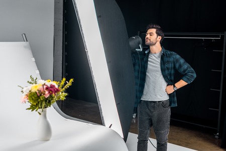 handsome young photographer working with lighting equipment and photographing beautiful flowers in...