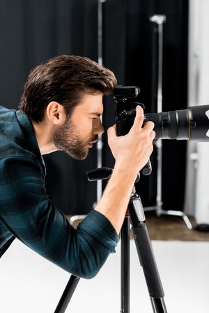 side view of handsome young photographer working with professional photo camera in studioの写真素材