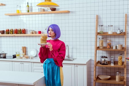 selective focus of beautiful housewife with purple hair holding plate with pancakes in kitchenの写真素材