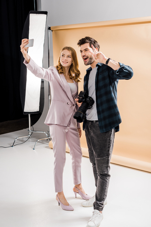 happy young photographer and beautiful smiling model taking selfie with smartphone in photo studioの写真素材
