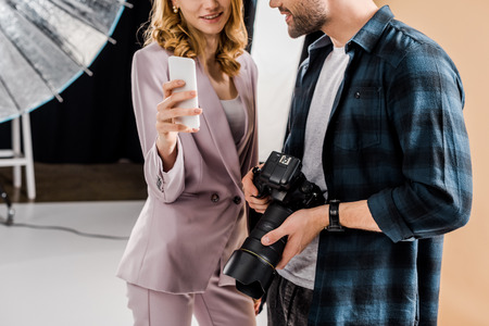 cropped shot of photographer and young woman using smartphone in photo studioの写真素材