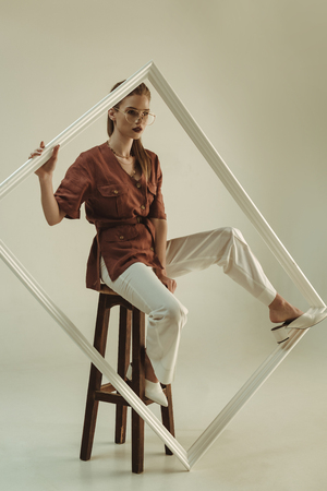beautiful young woman posing on stool with big white frameの写真素材