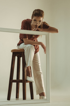 attractive fashionable woman posing on stool with big white frameの写真素材