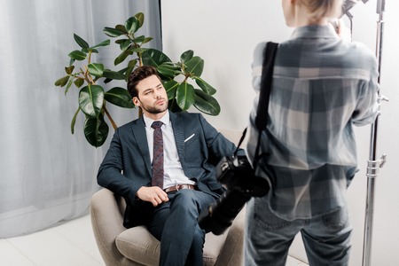 back view of photographer with camera looking at handsome businessman in photo studioの写真素材