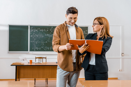 female teacher helping male student with assignment during lesson in classroomの写真素材