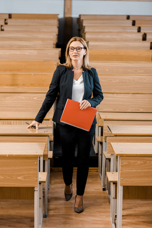 female university professor in formal wear holding journal and pen in classroomの写真素材