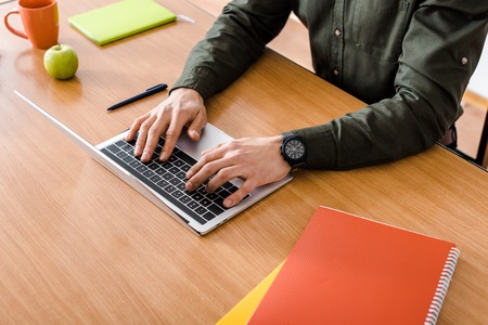 cropped view of male student using laptop at desk with notebooksの写真素材