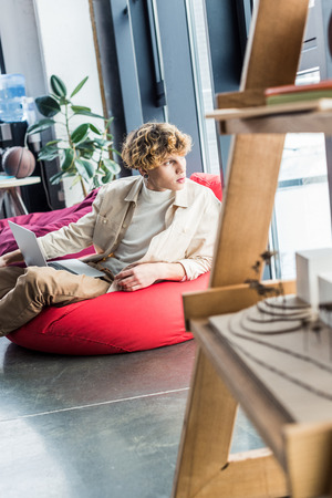 handsome casual businessman sitting in bean bag chair while using laptop in loft officeの写真素材