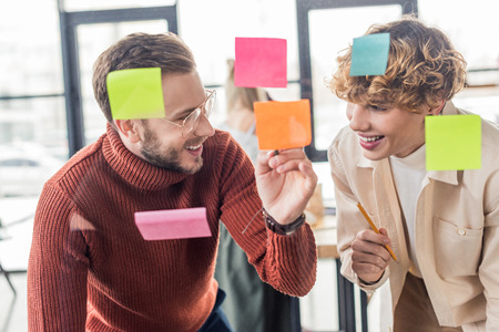 selective focus of handsome casual businessmen putting colorful sticky notes on glass window in...