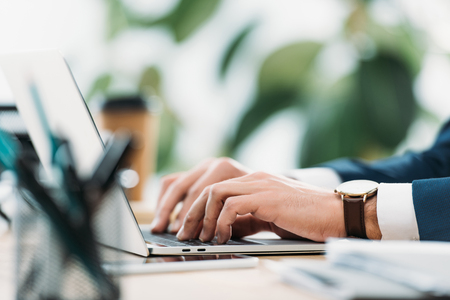 cropped view of businessman at table with laptop and typing in officeの写真素材