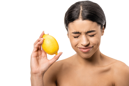young naked african american woman with closed eyes holding lemon and frowning isolated on whiteの写真素材