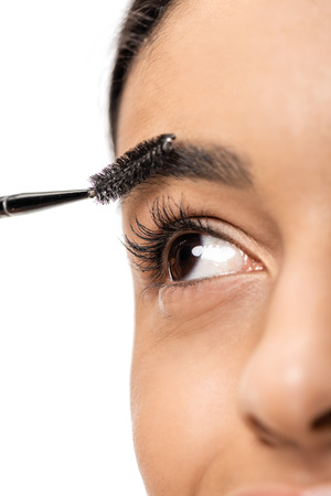 close-up view of beautiful young african american woman correcting eyebrow with brush isolated on whiteの写真素材