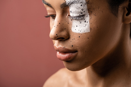 sensual african american woman with creative body art on face looking down isolated on brownの写真素材
