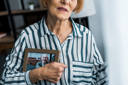 partial view of senior woman holding frame with man on photograph at homeの写真素材