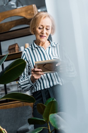 selective focus of senior woman looking at picture frame at home