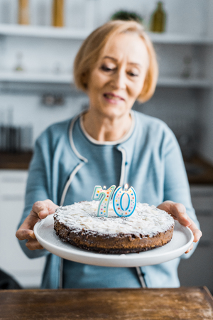 selective focus of cake with '70' sign on top and senior woman on background during birthday celebrationの写真素材