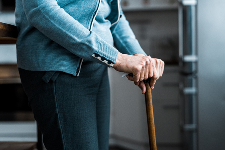 cropped view of senior woman leaning on wooden walking stick at homeの写真素材