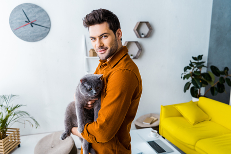 handsome smiling man holding british shorthair cat at homeの写真素材