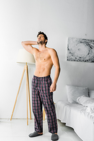 shirtless tired man in pajama pants standing with headache in morningの写真素材