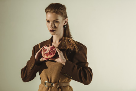 attractive woman holding half of fresh pomegranate isolated on beigeの写真素材