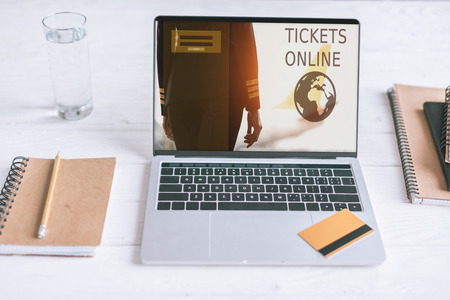 laptop with tickets online website on screen and credit card on wooden desk