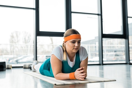 pensive overweight girl relaxing on fitness mat in gymの写真素材