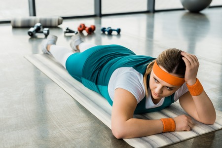 exhausted overweight girl lying on fitness mat in gym