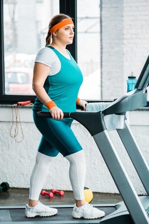 focused overweight girl workouting on treadmill in gym