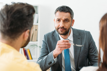 selective focus of advisor sitting at table and holding glasses near investors in officeの写真素材