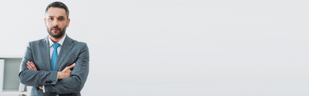 handsome businessman in grey suit standing with crossed arms in officeの写真素材