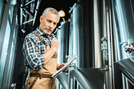male brewer in working overalls holding notepad in breweryの写真素材