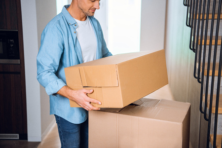 cropped view of man holding box in hands and smiling in new homeの写真素材