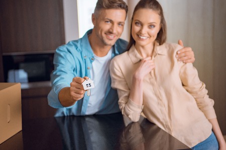selective focus of house shaped key chain in hand of handsome man hugging wife