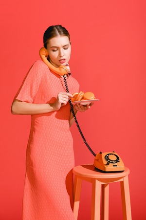 beautiful woman with macaroons and vintage rotary phone isolated on living coral. Color of the year 2019 conceptの写真素材
