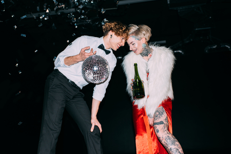 man holding disco ball and standing near woman with bottle of alcohol drink on party on black backgroundの写真素材