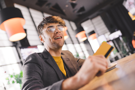 handsome man in glasses sitting at bar counter while holding credit card in cafeの写真素材