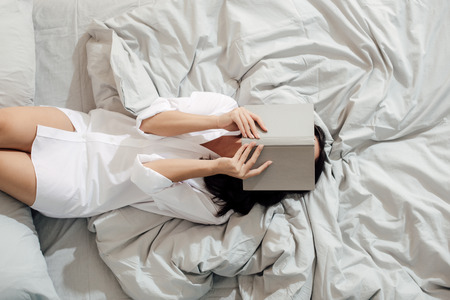 top view of young woman in white shirt lying with book on face in bed