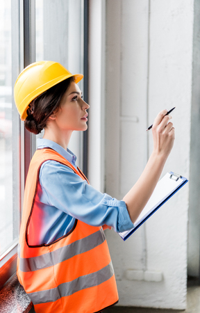 female firefighter in helmet and uniform holding clipboard and pen in handsの写真素材