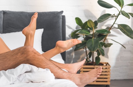 cropped view of woman and man lying in bed at homeの写真素材