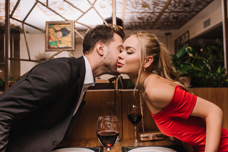 attractive girl kissing cheek of man in restaurant on valentines dayの写真素材