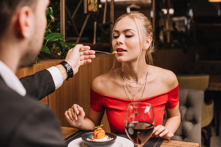 boyfriend feeding woman with sweet dessert in restaurantの写真素材