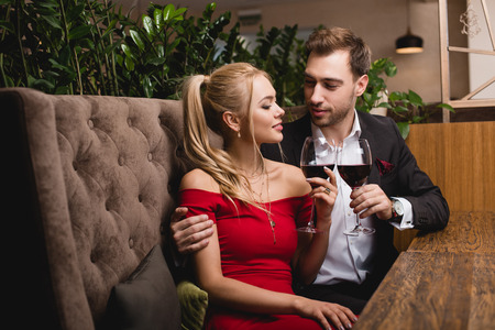 attractive woman toasting with glass of red wine with boyfriend in restaurant