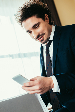 handsome businessman talking on smartphone and holding documents in hotel roomの写真素材
